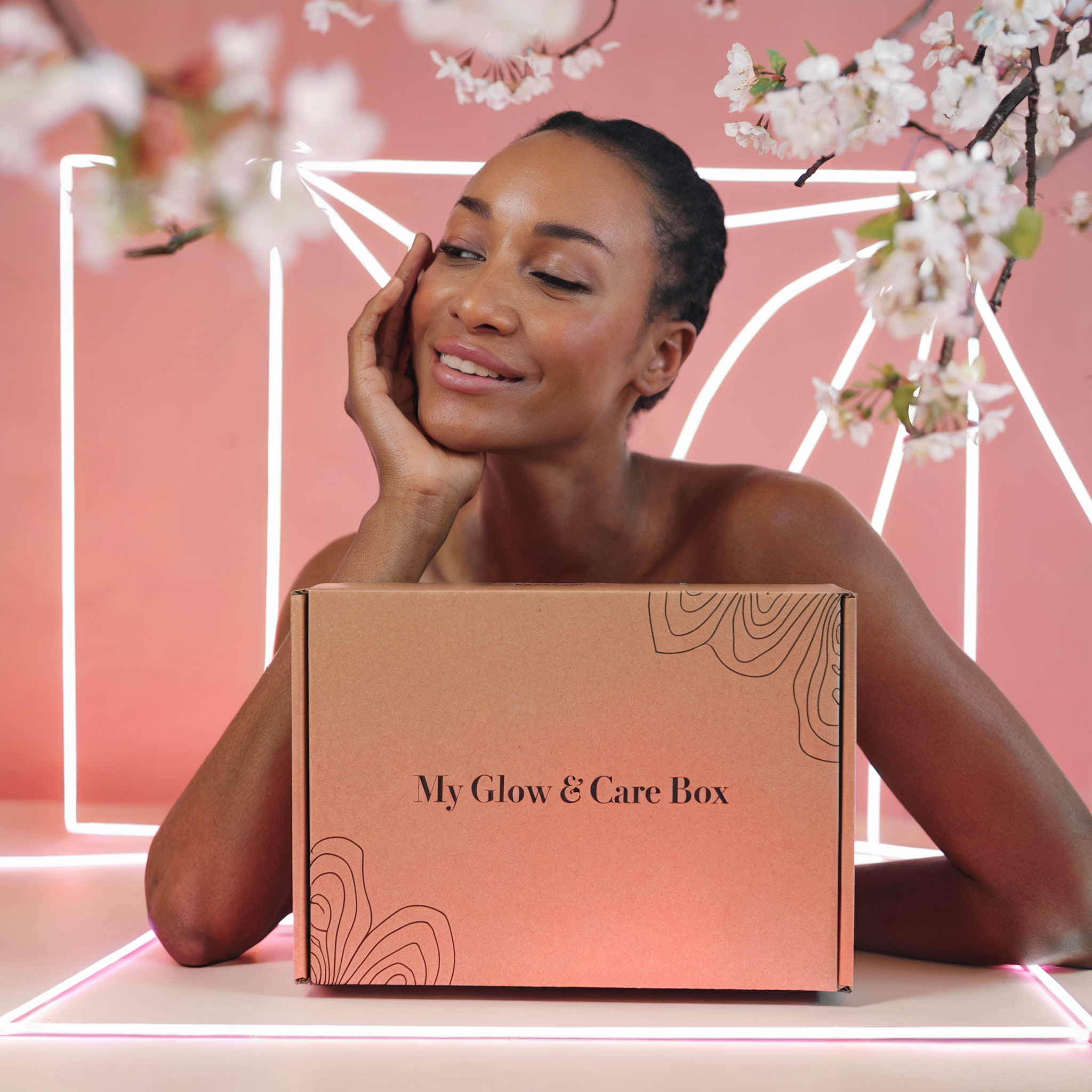 Femme africaine de 45 ans, souriante, devant une élégante My Glow & Care Box contenant 2 produits, un livret et du papier de soie